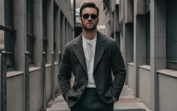 Man demonstrating effortless style hacks with a classic dark blazer, white crew neck t-shirt, and sunglasses, showcasing a sharp, minimal look.
